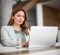 A imagem mostra uma mulher com roupas sociais usando um notebook no que parece ser um escritório. Ela aparenta ter um olhar confiante e seguro, pois está acessando um site que utiliza Wildcard SSL para aumentar a segurança dos dados.