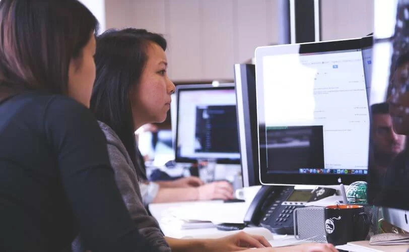 a imagem mostra duas mulheres em um escritório olhando para a tela de um computador. 