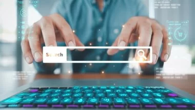 Uma pessoa de camisa clara digita em um teclado. Sobre a imagem, aparece uma barra de pesquisa com uma lupa escrito “search...”. A imagem é uma forma de representar a prática de black hat.