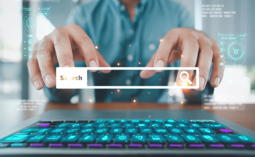 Uma pessoa de camisa clara digita em um teclado. Sobre a imagem, aparece uma barra de pesquisa com uma lupa escrito “search...”. A imagem é uma forma de representar a prática de black hat.