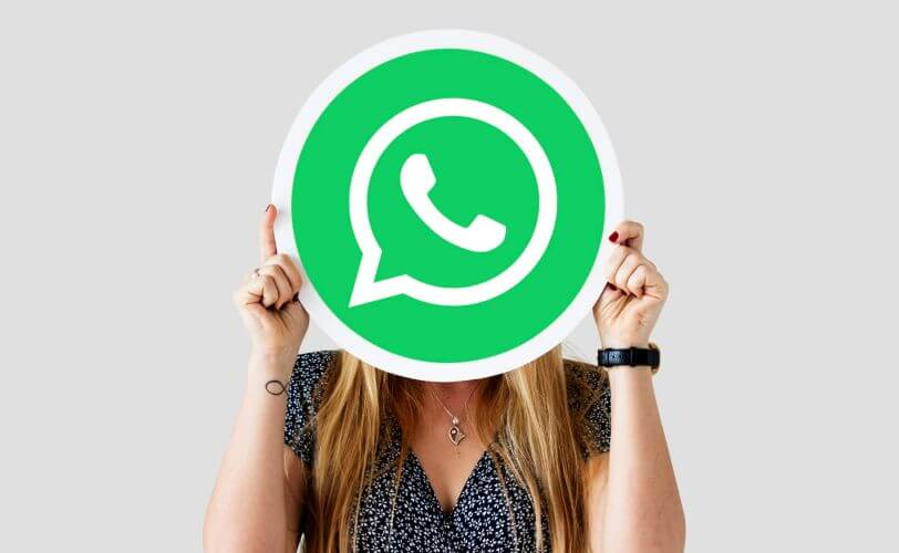 Alt text: na imagem há uma mulher com o logo do WhatsApp em frente ao seu rosto. A imagem faz referência ao conteúdo de botão do whatsapp em sites de ecommerce.