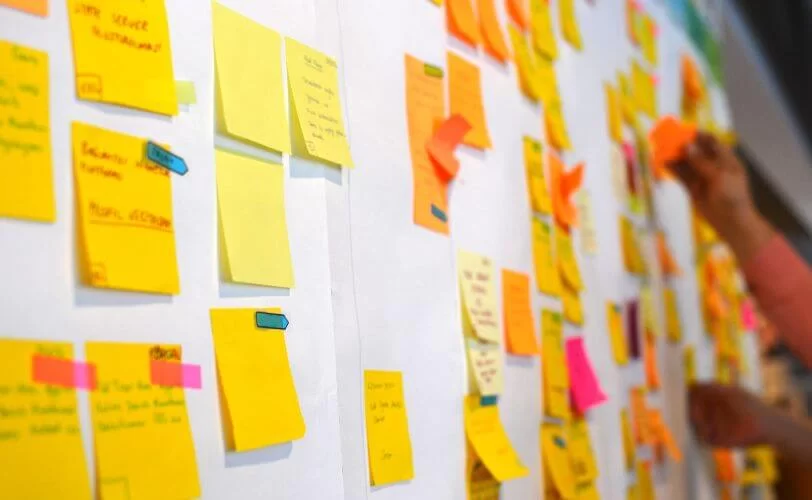 há uma parede branca com diversos post-its, fazendo referência ao trabalho de Product Owner e sua visão global de um produto