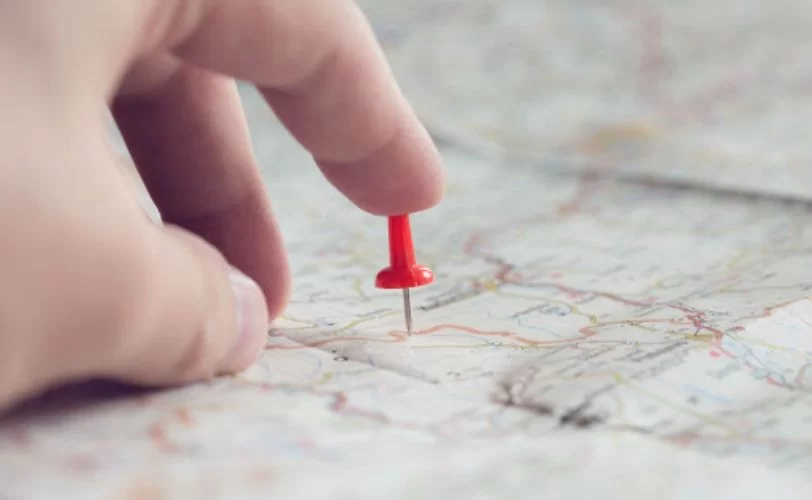 a imagem mostra um mapa e a mão de uma pessoa colocando um alfinete para marcar um local, para ilustrar as metas e objetivos traçados em um roadmap