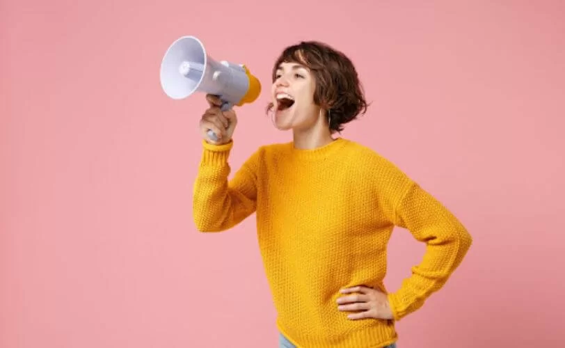 a imagem mostra uma mulher frente a uma parede rosa com um megafone. A imagem faz referência a personificação de marca.