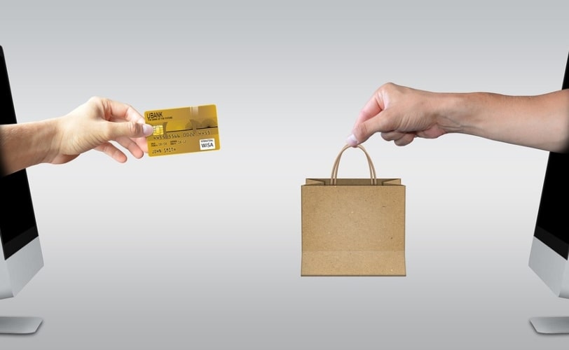 Na imagem há uma pessoa à esquerda que entrega um cartão e outra a direita que entrega uma sacola de compras, em ambas aparecem apenas o antebraço. O objetivo da imagem é compor o conteúdo sobre ciclo de vendas.