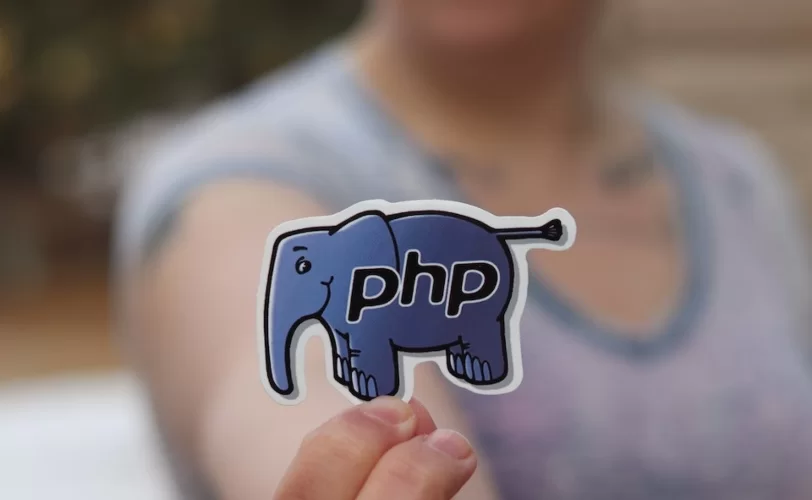 Imagem mostra uma pessoa segurando um adesivo de um elefante azul, mascote do PHP.
