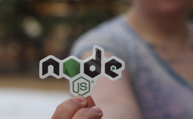 na imagem há uma mulher segurando um logo em papel do node.js. O logo está em destaque e o resto da paisagem está desfocado. 