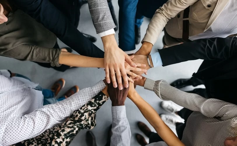 Visão área de um grupo estendendo suas mãos ao centro para demonstrar união em equipe. 