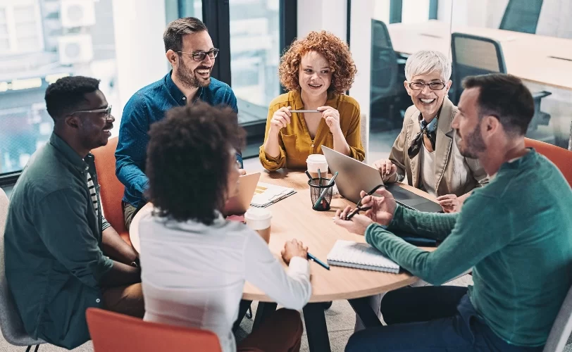 Na imagem pessoas estão ao sentados a uma mesa e estão conversando felizes.