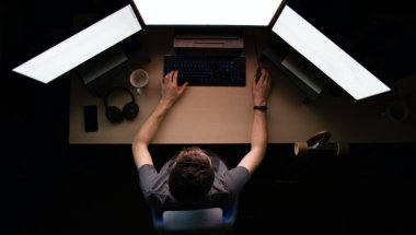 Na imagem, um homem está em frente a um computador com três telas.