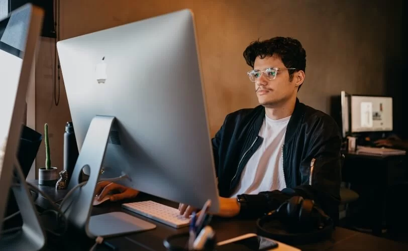 A imagem mostra um rapaz em frente a um mac da apple. 