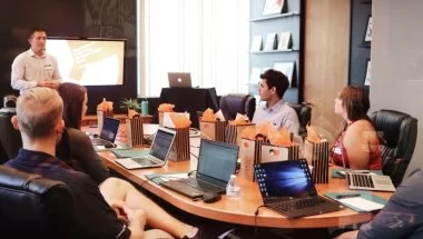 A imagem mostra uma sala de reuniões com várias pessoas.