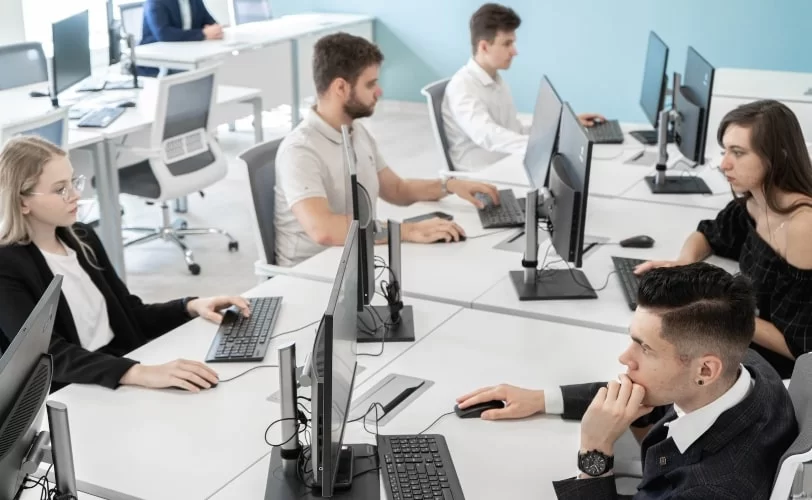 Imagem de um escritório com várias pessoas em frente a seus computadores. 