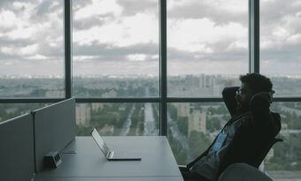 Na imagem está um homem sentado na mesa de um escritório.