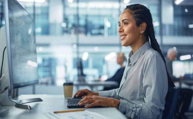 mulher programadora, em um escritório, sentada em frente a uma tela de computador. 