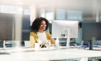 mulher sorridente frende a uma tela de computador em um escritório corporativo.