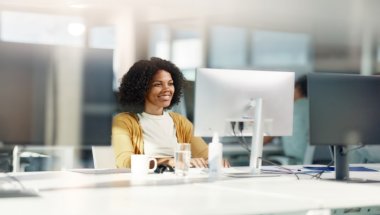 mulher sorridente frende a uma tela de computador em um escritório corporativo.