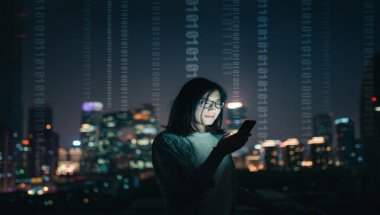 mulher usando celular e ao fundo uma cidade a noite.