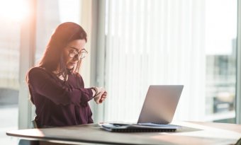 mulher olhando o relógio no seu pulso em um ambiente de trabalho. a imagem compõe o conteúdo sobre a técnica pomodoro.