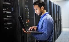 Homem com laptop em frente a um servidor para manutenção, segurança cibernética e verificação de internet.
