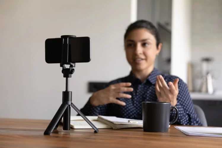 mulher gesticulando em frente a um celular em um mini tripé. 