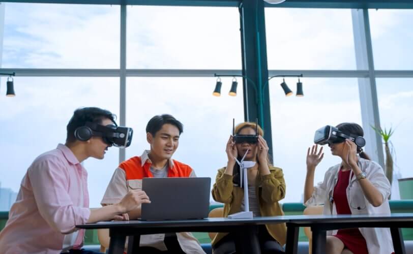 na imagem quatro pessoas em volta da mesa, e três estão com óculos de realidade virtual. 