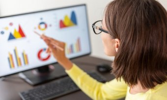 mulher em frente a uma tela de computador apontando para um dashboard com vários gráficos.
