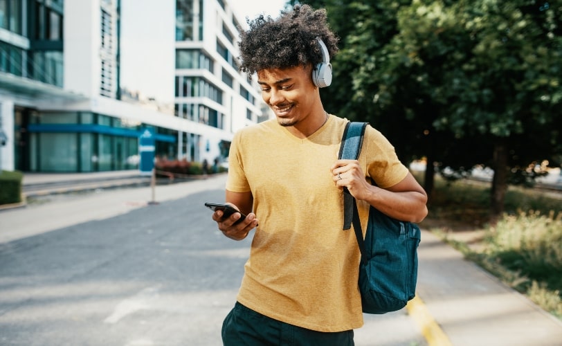 Rapaz com uma mochila nas costas, no meio da rua, olhando seu smartphone
