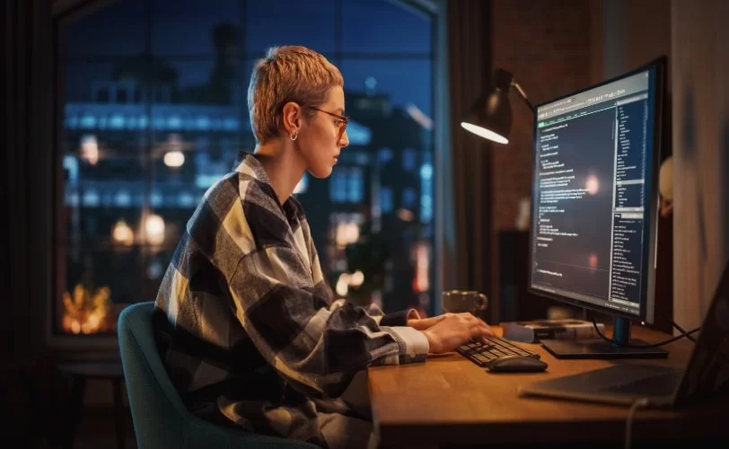 Mulher sentada frente a um computador e na tela há um editor de código. 