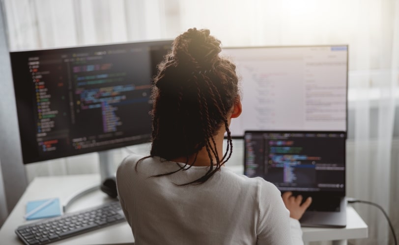 mulher sentada em frente a três telas de computador em ambas há um editor de código. 