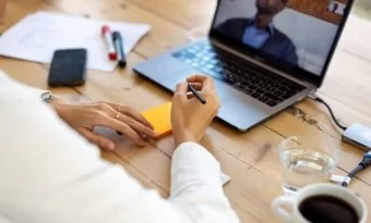 homem em uma mesa de escritório, frente a um notebook e escrevendo em um post-it.