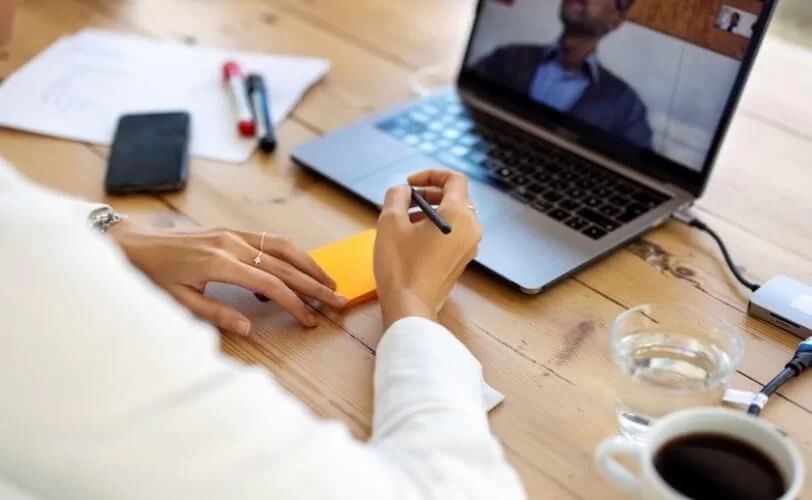 homem em uma mesa de escritório, frente a um notebook e escrevendo em um post-it.