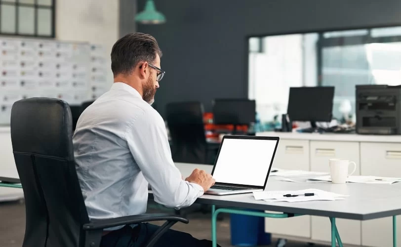 Homem sentado a uma escrivaninha, digitando em um notebook. 