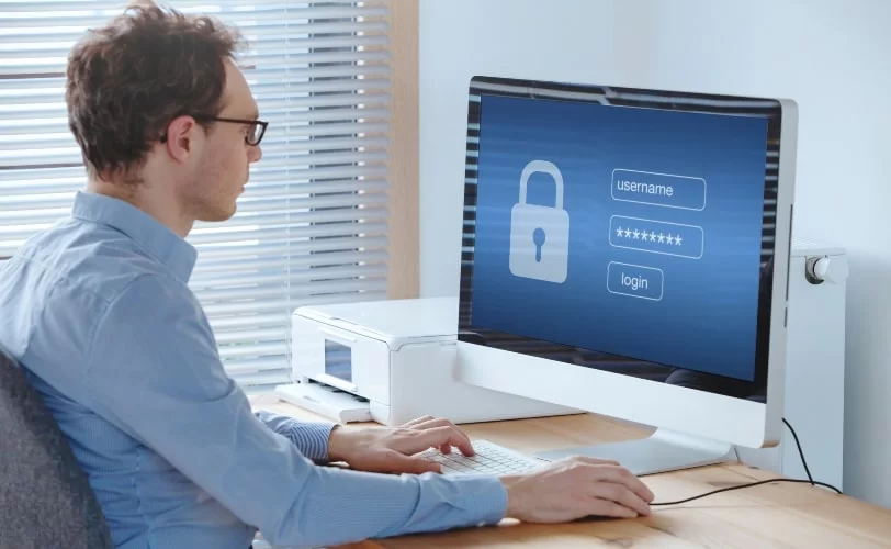 Homem sentado em frente a uma tela de computador, e nela há uma página de login e um cadeado denotando segurança na web. 