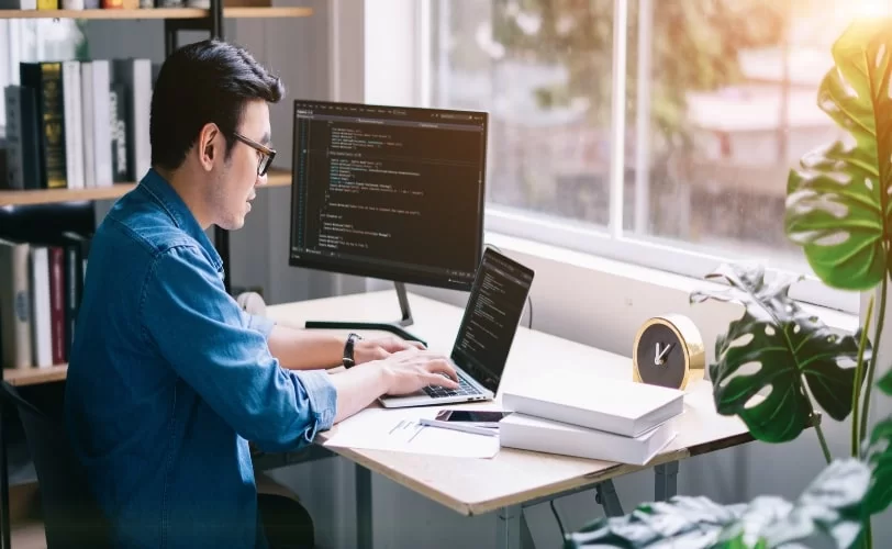 Homem criando algoritmos em seus computadores sobre mesa de madeira