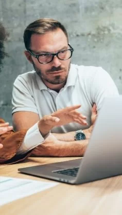 Um homem e uma mulher conversando enquanto apontam para a tela de um computador.