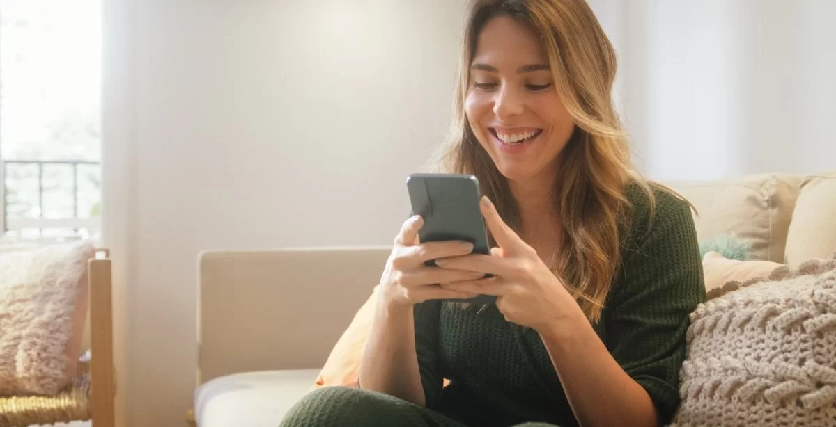A imagem mostra uma mulher loira mexendo no celular. Ela provavelmente foi impactada pela publicação de uma empresa que pensou em como crescer no Instagram, aplicando algumas técnicas para aumentar alcance e engajamento.