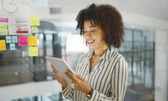 Mulher sorrindo e olhando para um tablet. A imagem compõe o conteúdo sobre extensões para o google chrome.