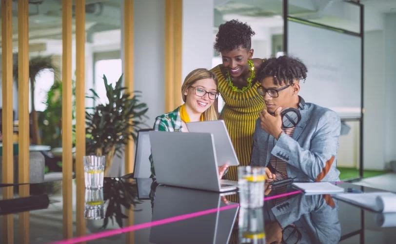 Na imagem, estão três pessoas conversando e olhando para uma tela de tablet. A foto compõe o conteúdo sobre impactos das IAs nas estratégias de SEO. 