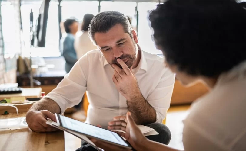 Mulher e homem olhando para a tela de um tablet. A imagem é do artigo sobre SEO e inteligência artificial. 