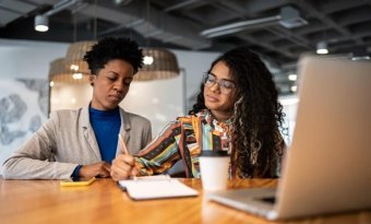 Duas mulheres sentadas frente a uma mesa de escritório.