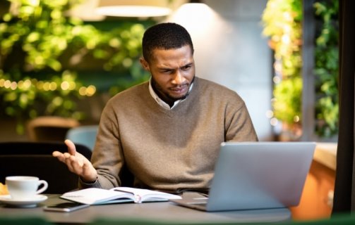 Homem fazendo gesto de indignação ao olhar para a tela do notebook. A imagem compõe o artigo sobre o que é o SPAM nas estratégias e e-mail marketing.