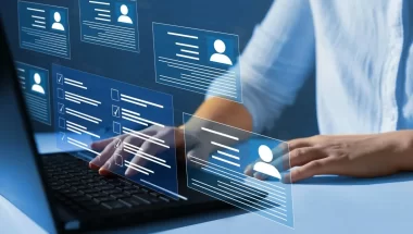 A imagem mostra um homem em um escritório mexendo em um notebook. O rosto dele não aparece. Da tela, surgem várias pequenas telas, algumas simulando perfis de redes sociais e outras com informações escritas e caixas de confirmação.