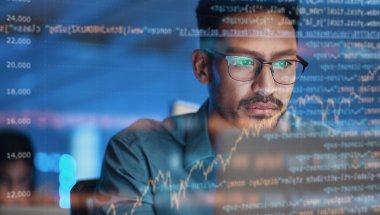 A imagem mostra um homem de óculos em seu ambiente de trabalho. Ele está diante de uma tela com gráficos e diversas linhas de código, indicando que possivelmente está usando o Domain-Driven Design para desenvolver um software.