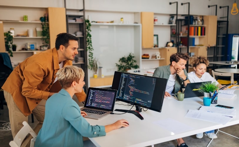 Na imagem há um escritório com 4 pessoas e na esquerda há um rapaz desenvolvedor conversando com uma mulher sobre implementação de CI e CD.
