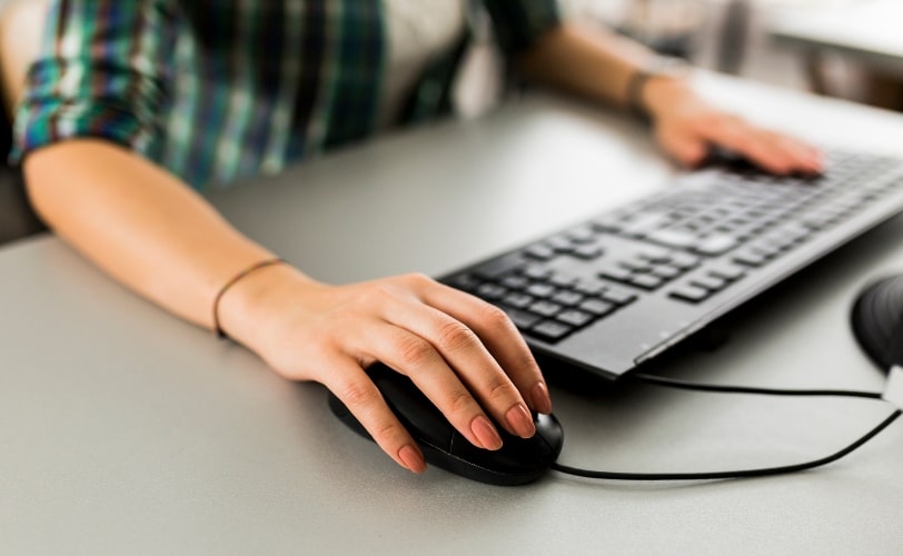a imagem mostra uma mulher em frente a um computador, digitando e segurando o mouse.  