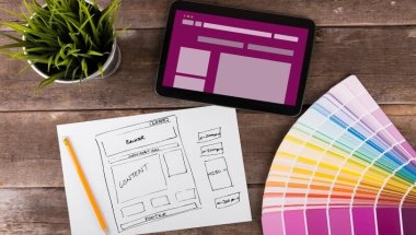 A imagem mostra rascunhos de telas de aplicativo desenhadas à mão, representando o processo de wireframe (etapa essencial do UX/UI design). Sobre a mesa estão canetas coloridas, notas adesivas e um notebook, simbolizando a fase criativa e analítica do desenvolvimento de produtos digitais. As setas entre as telas indicam o fluxo de navegação do usuário, demonstrando como ideias são estruturadas antes da implementação. Essa cena reflete o equilíbrio entre design funcional e experiência do usuário, fundamentais para criar interfaces intuitivas e eficientes.