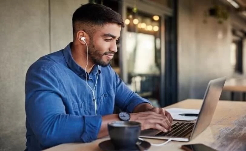 homem com fones de ouvidos mexendo no computador e sorrindo 
