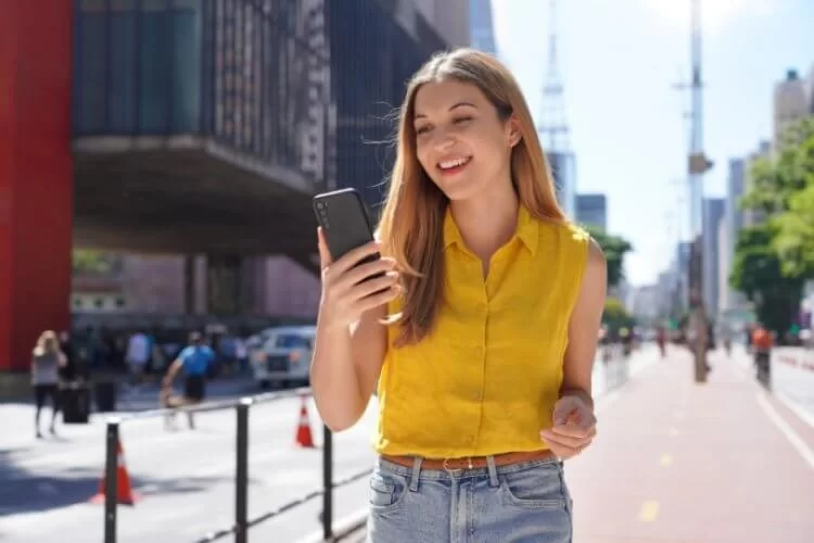 mulher andando na rua e vendo o celular