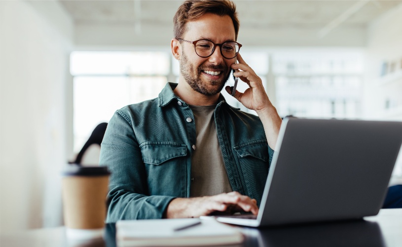 Homem conversando no celular diante de um laptop